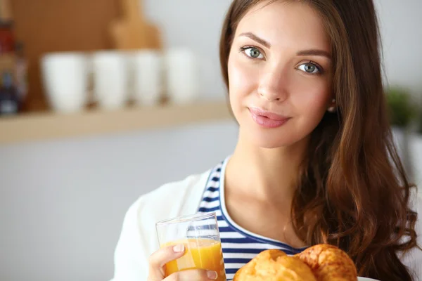 Mujer joven con vaso de jugo y pasteles de pie en la cocina . —  Fotos de Stock