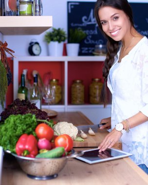 Mutfakta yemek yapmak için tablet bilgisayar kullanan genç bir kadın.