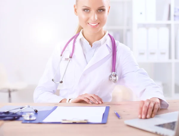 Bella giovane sorridente medico femminile seduto alla scrivania e la scrittura. — Foto Stock