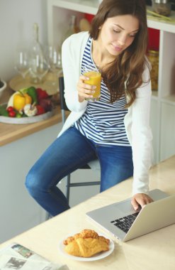 Dizüstü bilgisayar kullanarak ve mutfakta oturmuş çekici genç kadın