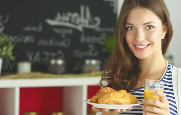 Mujer joven con vaso de jugo y pasteles de pie en la cocina . —  Fotos de Stock