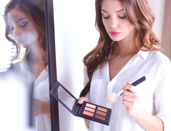 Genç ve güzel bir kadın aynanın yanında makyaj yapıyor.