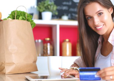 Gülümseyen kadın mutfakta tablet ve kredi kartı kullanarak alışveriş online