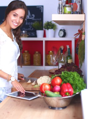 Mutfakta yemek yapmak için tablet bilgisayar kullanan genç bir kadın.