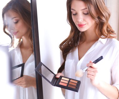 Genç ve güzel bir kadın aynanın yanında makyaj yapıyor.