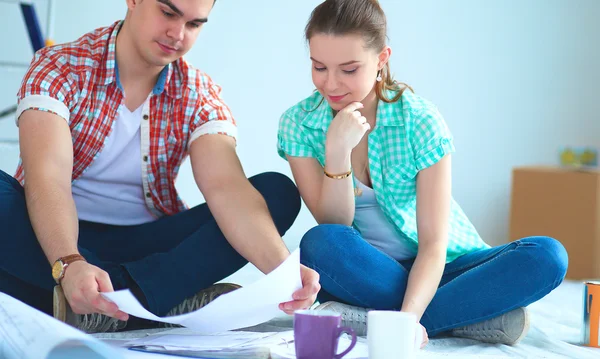 Pareja joven sentada en el piso con plano de apartamento — Foto de Stock