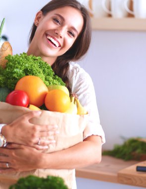 Elinde sebzeli alışveriş torbası tutan genç bir kadın.