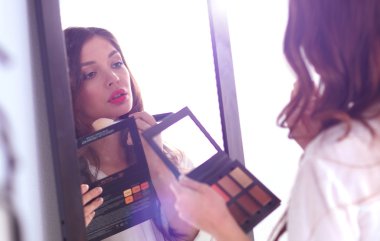 Genç ve güzel bir kadın aynanın yanında makyaj yapıyor.