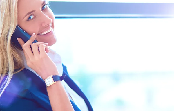 Businesswoman standing against office window talking on mobile phone