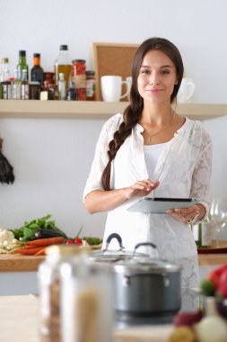 Mutfakta yemek yapmak için tablet bilgisayar kullanan genç bir kadın. .