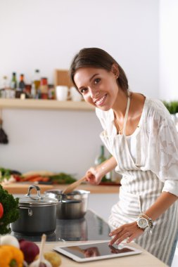 Mutfakta yemek yapmak için tablet bilgisayar kullanan genç bir kadın. .