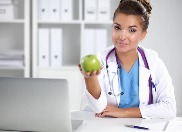 Mão médica feminina segurando uma maçã verde, sentada na mesa — Fotografia de Stock