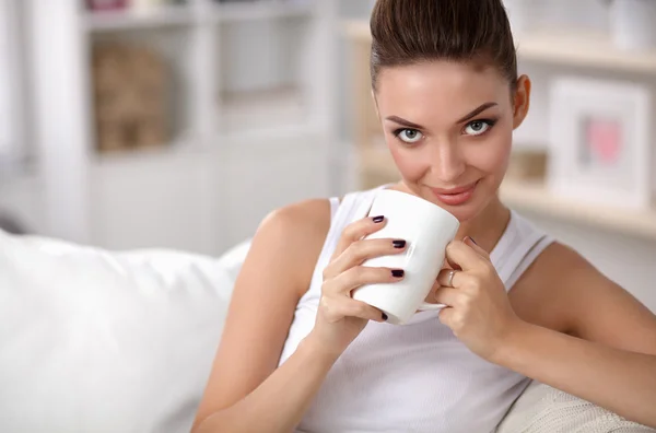 Retrato de una joven hermosa mujer con una taza en el sofá en casa —  Fotos de Stock