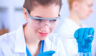 Kadın araştırmacı, beyaz arka planda izole edilmiş ilaç şişeleri ve mataralarla çevrili.