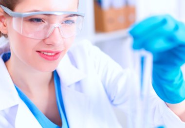 Kadın araştırmacı, beyaz arka planda izole edilmiş ilaç şişeleri ve mataralarla çevrili.