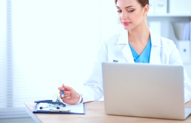 Güzel, genç, gülümseyen bayan doktor masada oturuyor ve yazıyor..