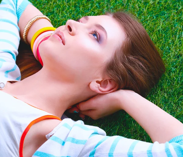Schöne junge Frau hält die Hände hinter dem Kopf und liegt auf dem grünen Gras — Stockfoto