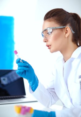 Kadın araştırmacı, beyaz arka planda izole edilmiş ilaç şişeleri ve mataralarla çevrili.