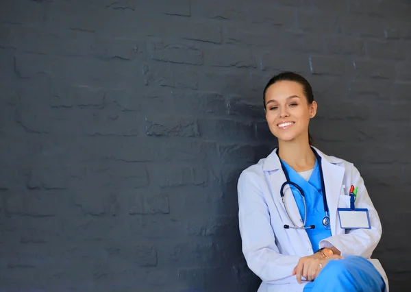 Young woman doctor sitting near wall — Stock Photo, Image