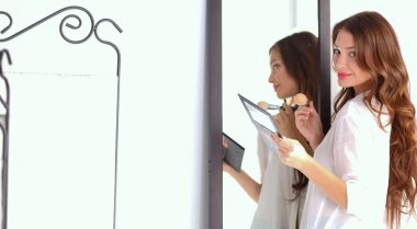 Genç ve güzel bir kadın aynanın yanında makyaj yapıyor.