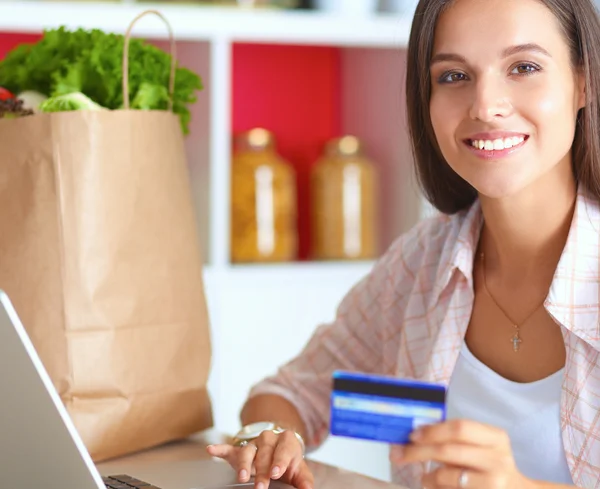 Mulher sorrindo compras on-line usando tablet e cartão de crédito na cozinha — Fotografia de Stock