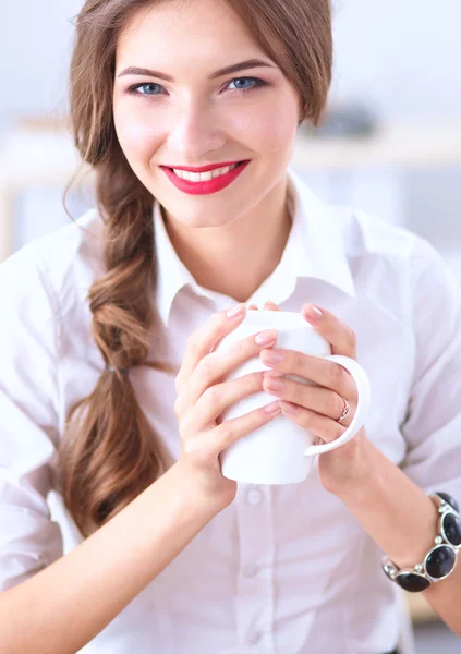 Joven mujer de negocios sentada en el escritorio con taza en la oficina —  Fotos de Stock