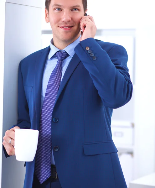 Hombre de negocios sonriente de pie y utilizando el teléfono móvil —  Fotos de Stock