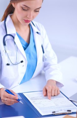 Güzel, genç, gülümseyen bayan doktor masada oturuyor ve yazıyor..