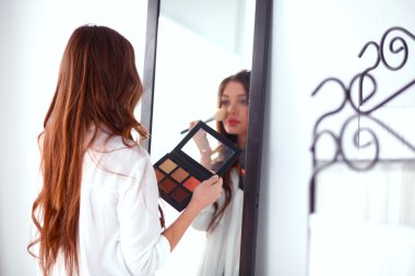 Genç ve güzel bir kadın aynanın yanında makyaj yapıyor.