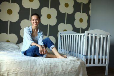 Yatakta çocuk karyolası yakın oturan genç kadın.