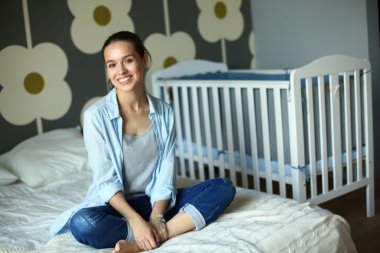 Yatakta çocuk karyolası yakın oturan genç kadın.