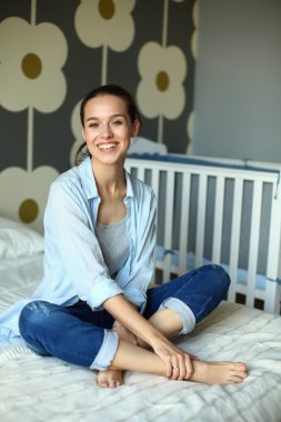 Yatakta çocuk karyolası yakın oturan genç kadın.