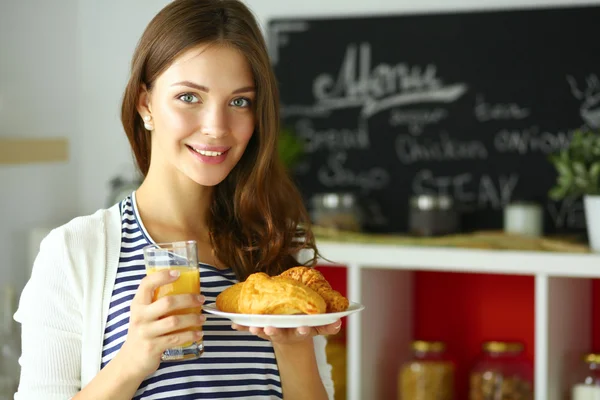 Mujer joven con vaso de jugo y pasteles de pie en la cocina . —  Fotos de Stock