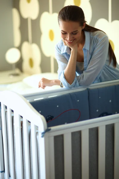 Young woman standing near childrens cot. — Stock Photo, Image
