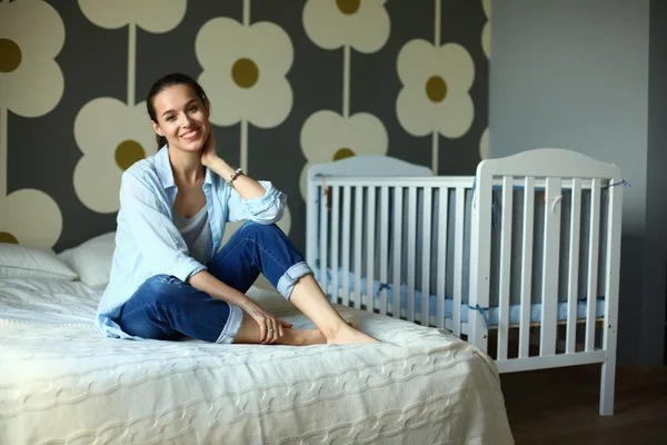 Jonge vrouw zittend op het bed in de buurt van childrens kinderbed. — Stockfoto