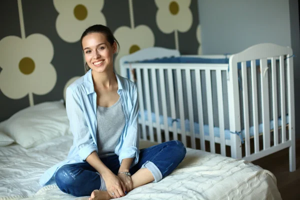 Jovem mulher sentada na cama perto do berço das crianças . — Fotografia de Stock