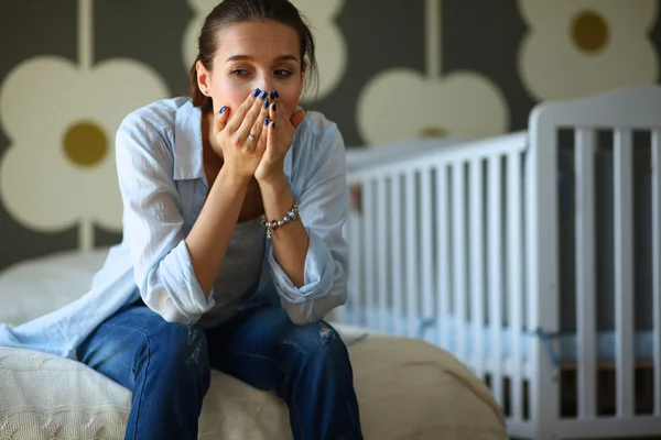 Unga trött kvinna som sitter på sängen nära barnens barnsäng. — Stockfoto