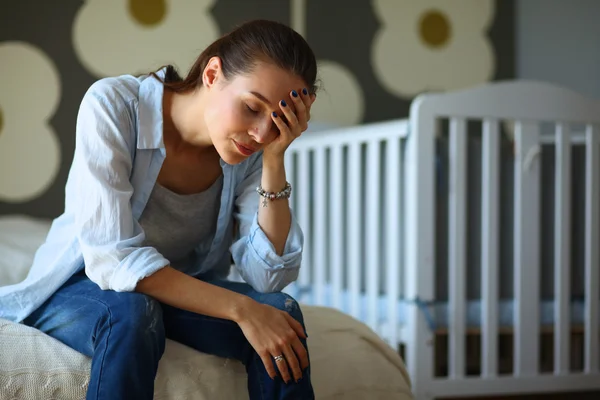 Unga trött kvinna som sitter på sängen nära barnens barnsäng. — Stockfoto