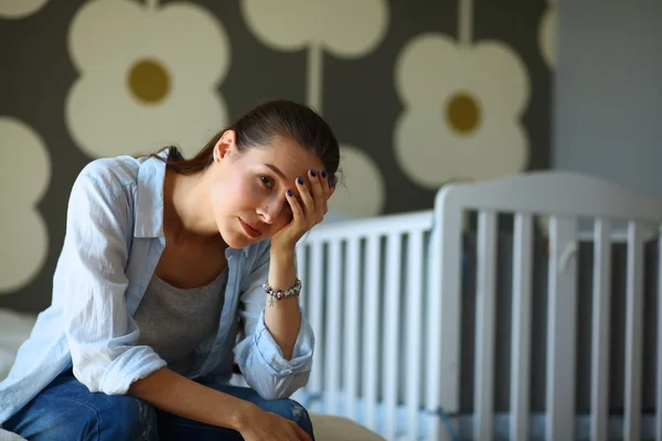 Unga trött kvinna som sitter på sängen nära barnens barnsäng. — Stockfoto