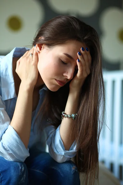 年轻疲惫的女子，坐在附近儿童床床上. — 图库照片