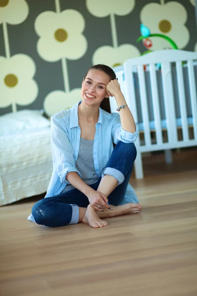 Young woman sitting on the floor near childrens cot. — Stock Photo, Image