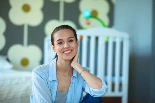 Jonge vrouw zittend op de vloer in de buurt van childrens kinderbed. — Stockfoto