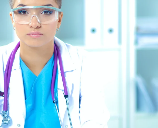 Hermosa joven sonriente doctora sentada en el escritorio y escribiendo. —  Fotos de Stock