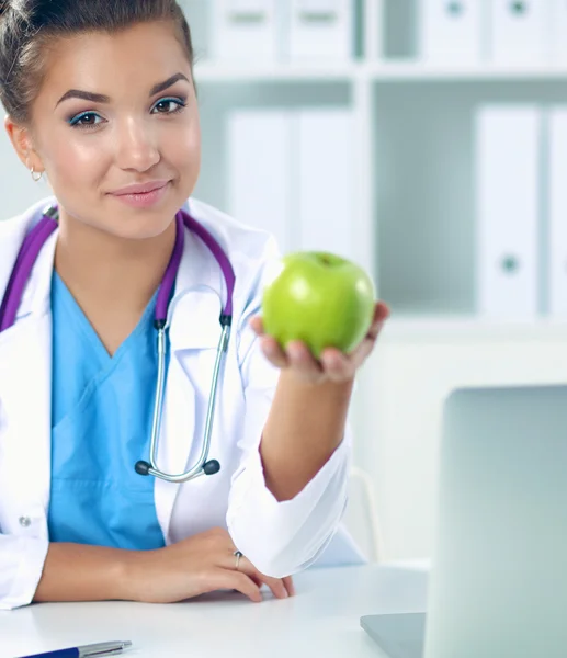 Mão médica feminina segurando uma maçã verde, sentada na mesa — Fotografia de Stock