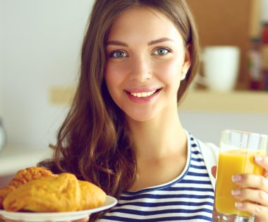 Mutfakta elinde meyve suyu ve kekle bekleyen genç bir kadın. .