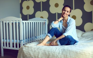 Yatakta çocuk karyolası yakın oturan genç kadın.