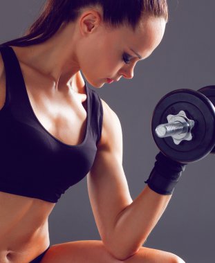 Atletik kadın dambıllarla kaslarını şişiriyor.