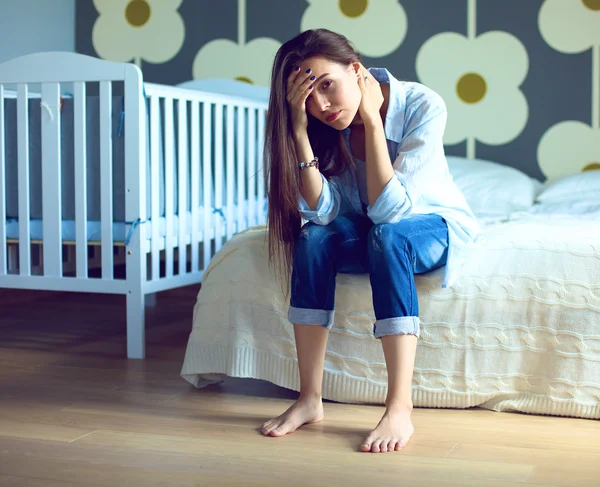 Unga trött kvinna som sitter på sängen nära barnens barnsäng. — Stockfoto