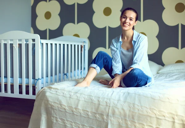 Junge Frau sitzt auf dem Bett in der Nähe von Kinderbett. — Stockfoto