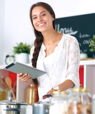 Mutfakta yemek yapmak için tablet bilgisayar kullanan genç bir kadın. .
